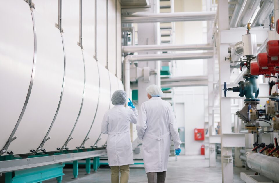Back view full length portrait of two factory workers wearing lab coats crossing production workshop, copy space