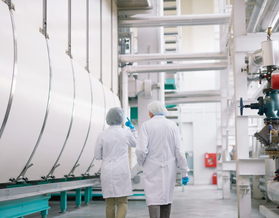 Back view full length portrait of two factory workers wearing lab coats crossing production workshop, copy space